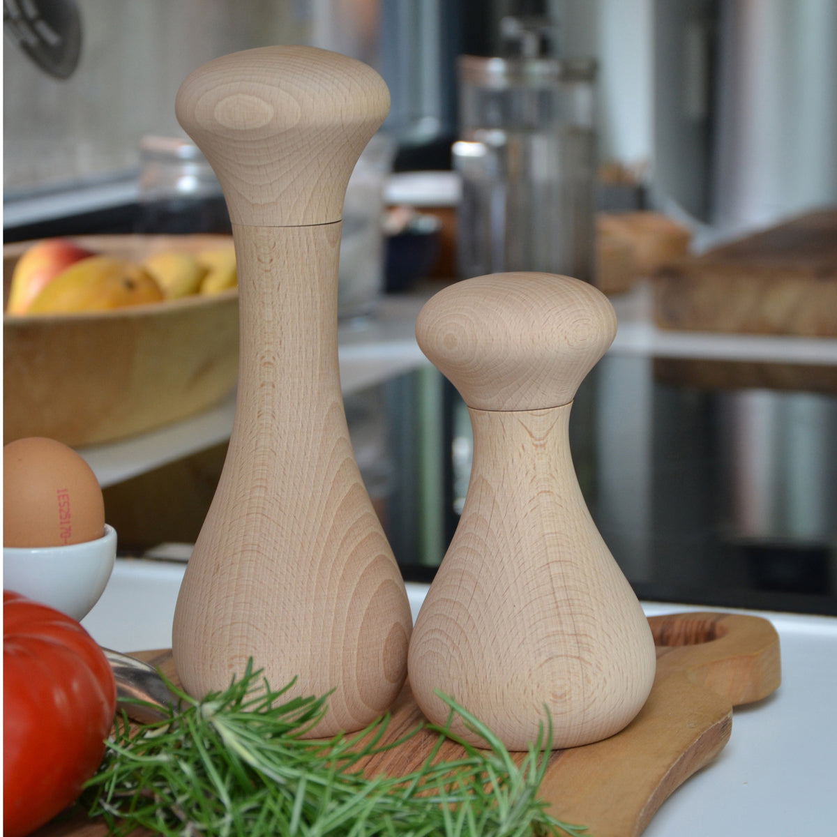 Two wooden salt and pepper shakers on a kitchen counter with herbs and eggs.
